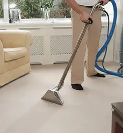 Professional carpet cleaner using a hot-water extraction wand and hose machine in a living room in Miami, FL.