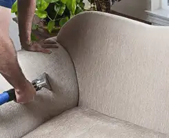 Professional upholstery cleaner deep-cleaning a fabric sofa with a handheld extraction tool and hose in Miami, FL.